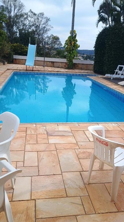 a swimming pool with two white chairs next to it at Casa com piscina para até 6 pessoas com duas camas de casal e sofá-cama casal in Serra Negra