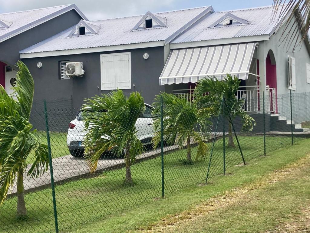 a fence in front of a house with a car parked in front at Le Petit Nid D'Ansbé in Anse-Bertrand