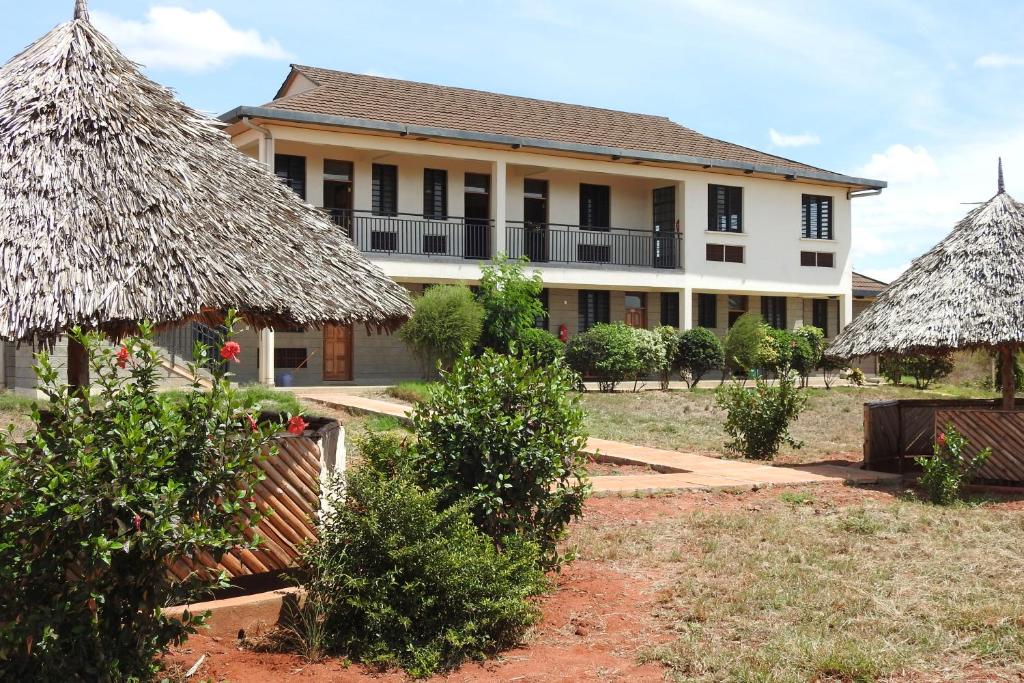 una casa con techos de paja y arbustos delante de ella en Voi Lutheran Guesthouse, en Voi