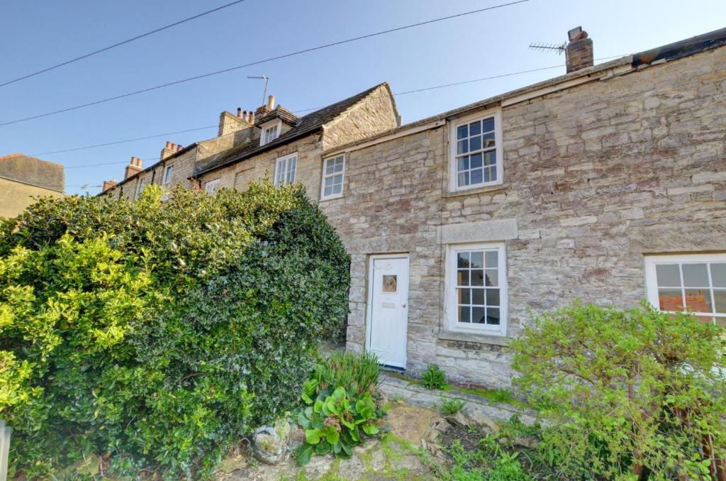 an old stone house with a white door at Holly Cottage in Swanage