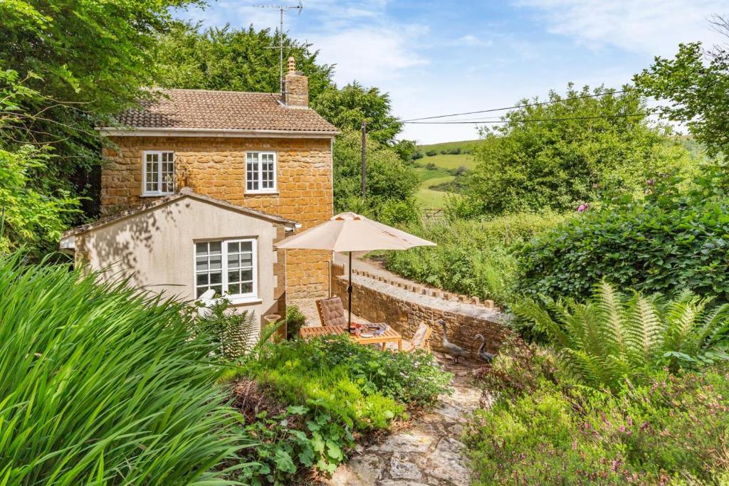 une maison en briques avec un parasol et une chaise dans l'établissement Rose Cottage - Stoke Abbott, à Stoke Abbott