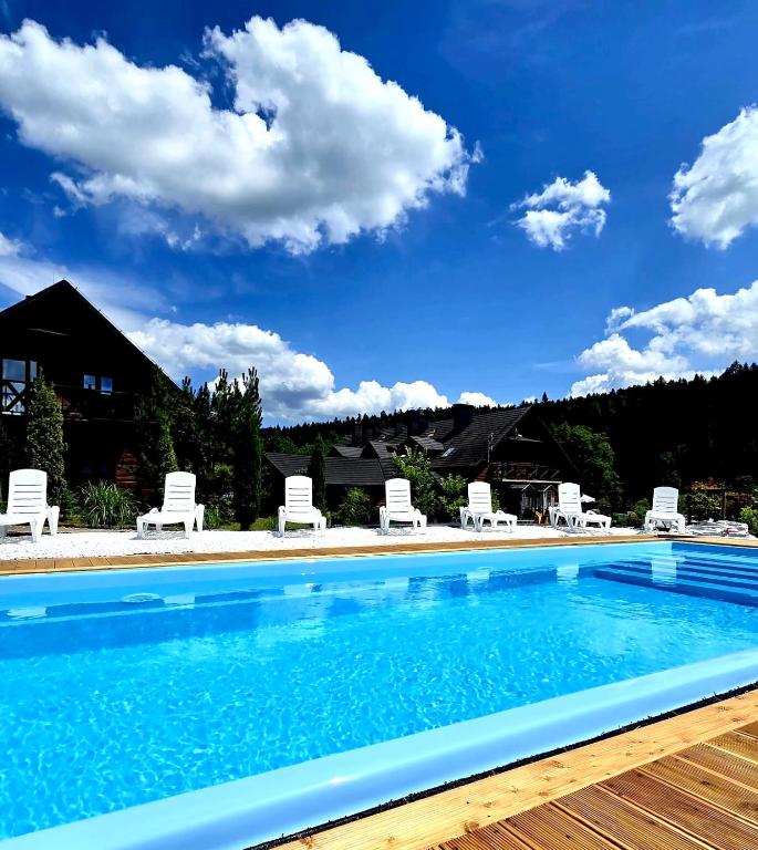 a swimming pool with chairs and a blue sky at Solny - Resort w Bieszczadach in Cisna