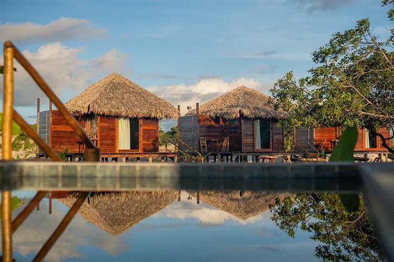 two huts with their reflections in a pool of water at AREIA BRANCA Chalés in Santo Amaro