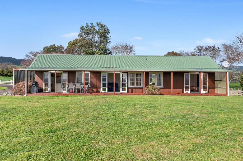 a red house with a green roof on a grass field at The Cottage - Rotorua Holiday Farmstay in Rotorua