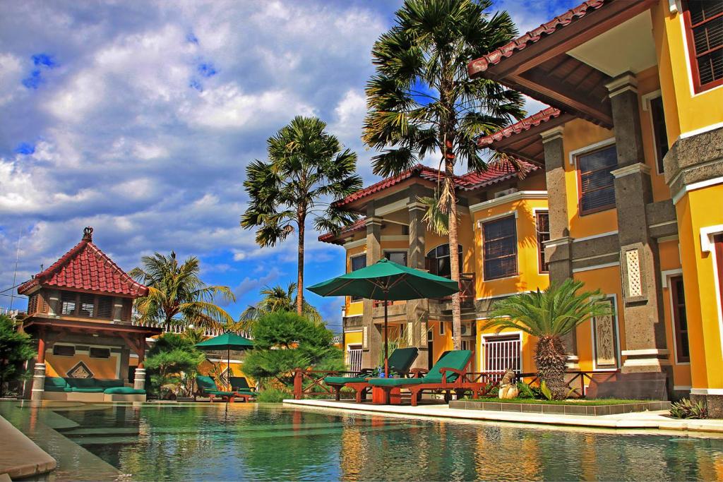 a resort swimming pool with chairs and umbrellas and palm trees at Apel Villa Sanur in Sanur