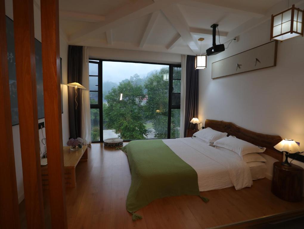 una camera da letto con un letto grande e una grande finestra di Zhangjiajie Southgate Flower Garden Lodge at the Park Entrance a Zhangjiajie