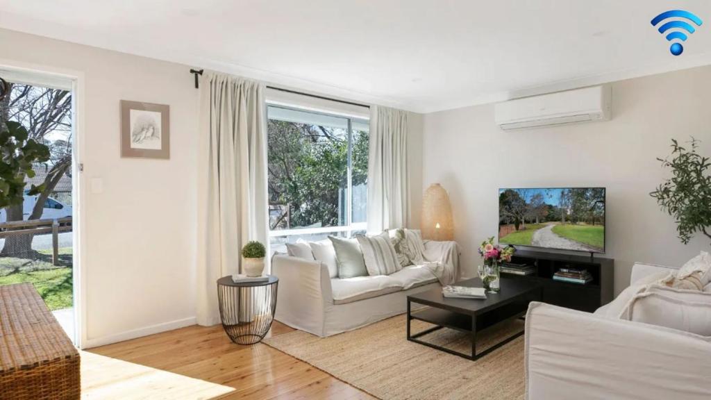 Una sala de estar con un sofá blanco y un televisor. en Bluebird Cottage, en Bowral