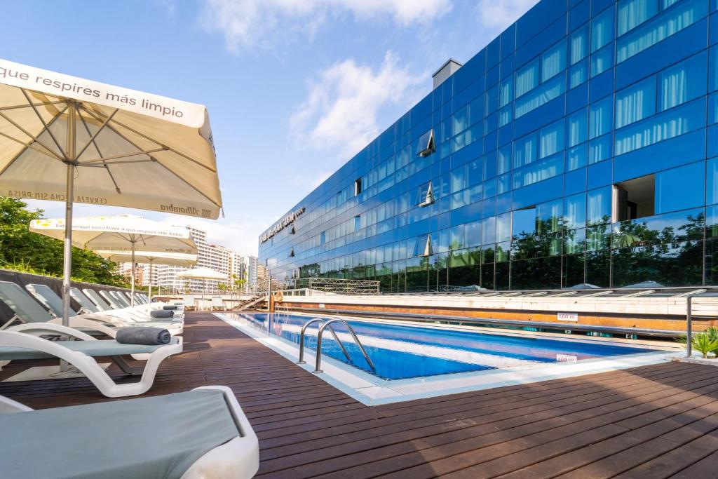 a swimming pool with chairs and an umbrella next to a building at Abba Playa Gijón in Gijón