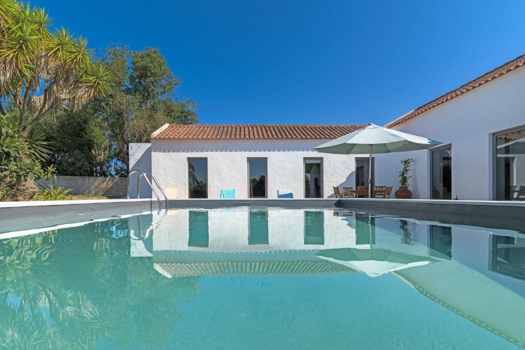 una piscina con un ombrellone accanto a una casa di Espaço Fataca - Sw Alentejano a São Teotónio