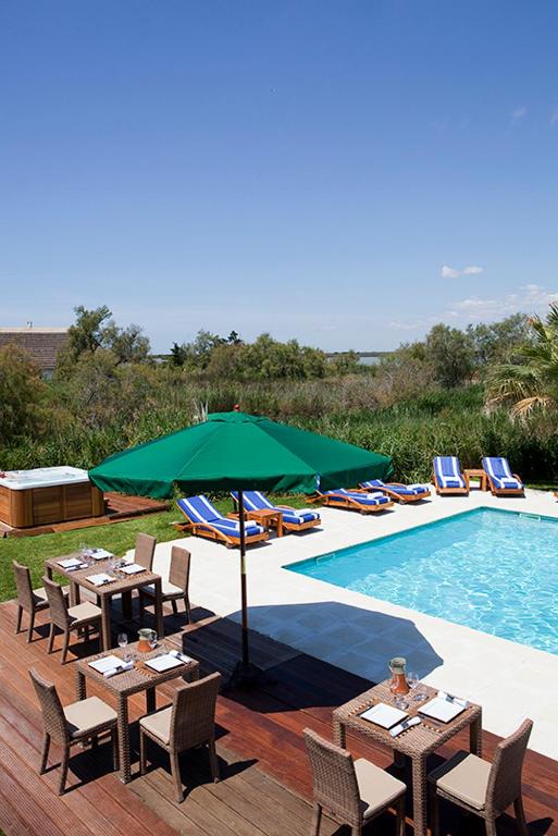 a pool with tables and chairs and a green umbrella at Mangio Fango Hotel et Spa in Saintes-Maries-de-la-Mer