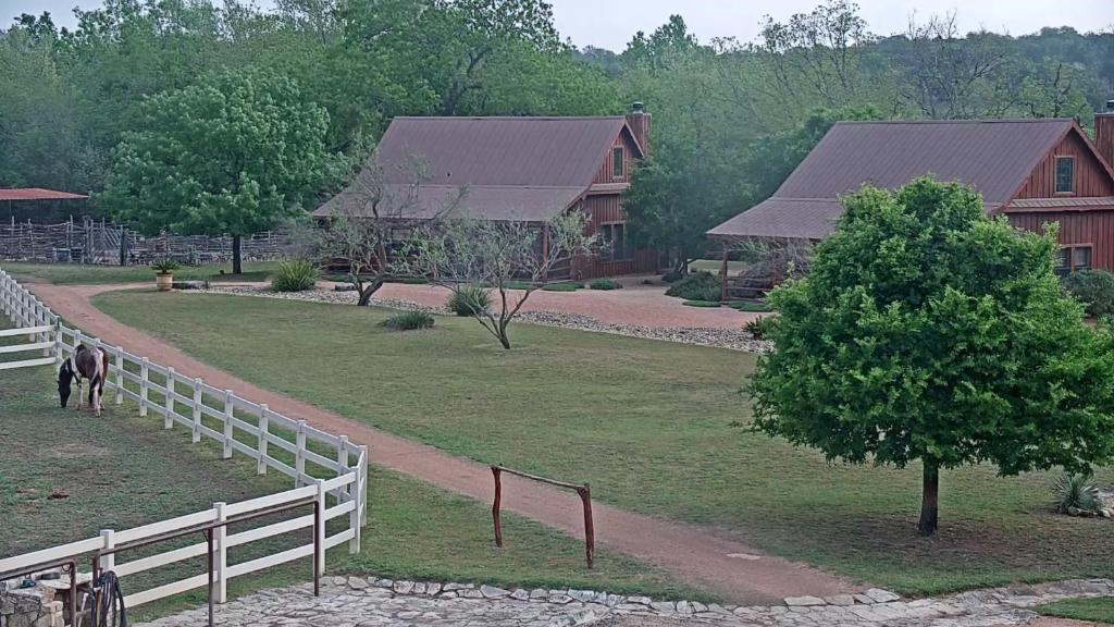 a white fence in front of a house with a tree at SisterCreek Ranch - Other Cabin in Boerne