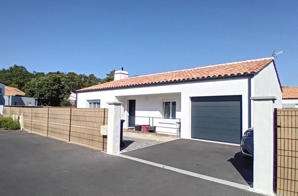 une maison blanche avec une clôture et un garage dans l'établissement Au pied de la forêt, à Saint-Jean-de-Monts