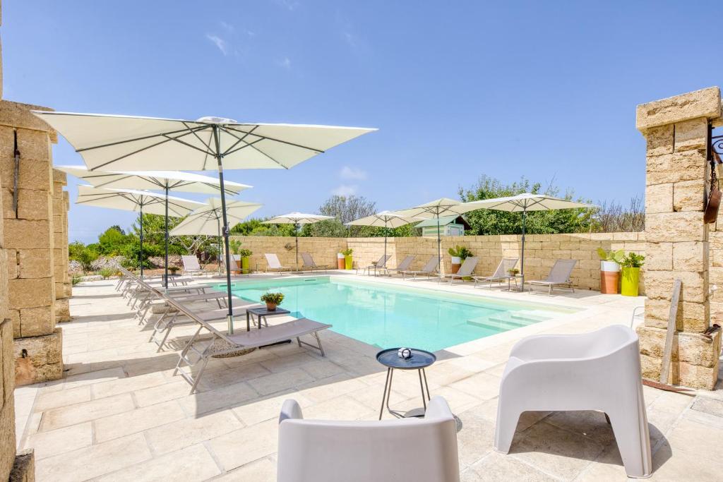 a swimming pool with white chairs and umbrellas at Tenuta Palmira agriturismo in Salve