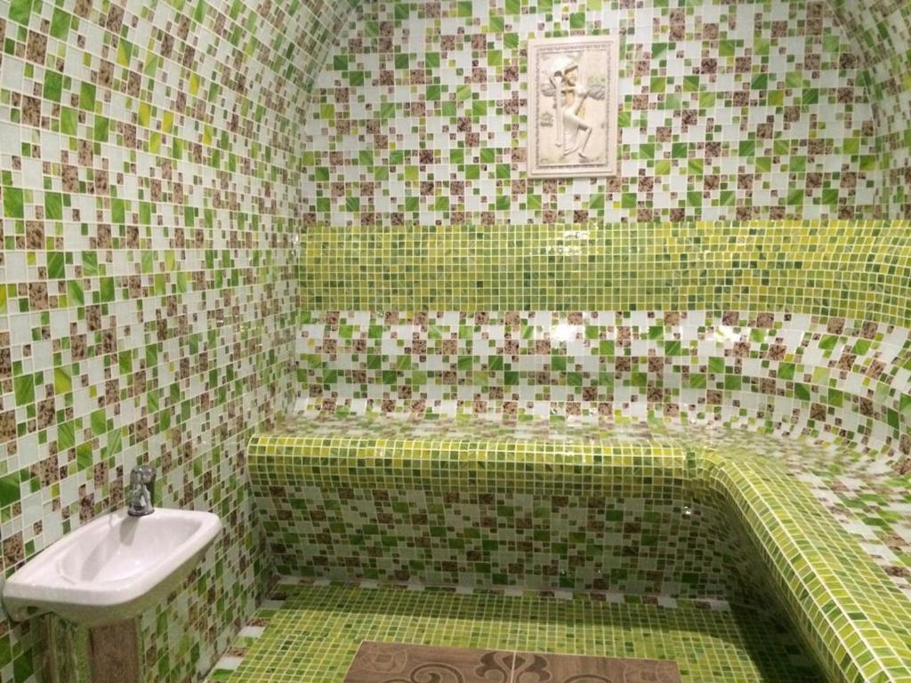 La salle de bains carrelée de couleur verte est pourvue d'un lavabo et d'une baignoire. dans l'établissement Gostinitsa Grand, à Kyzylorda