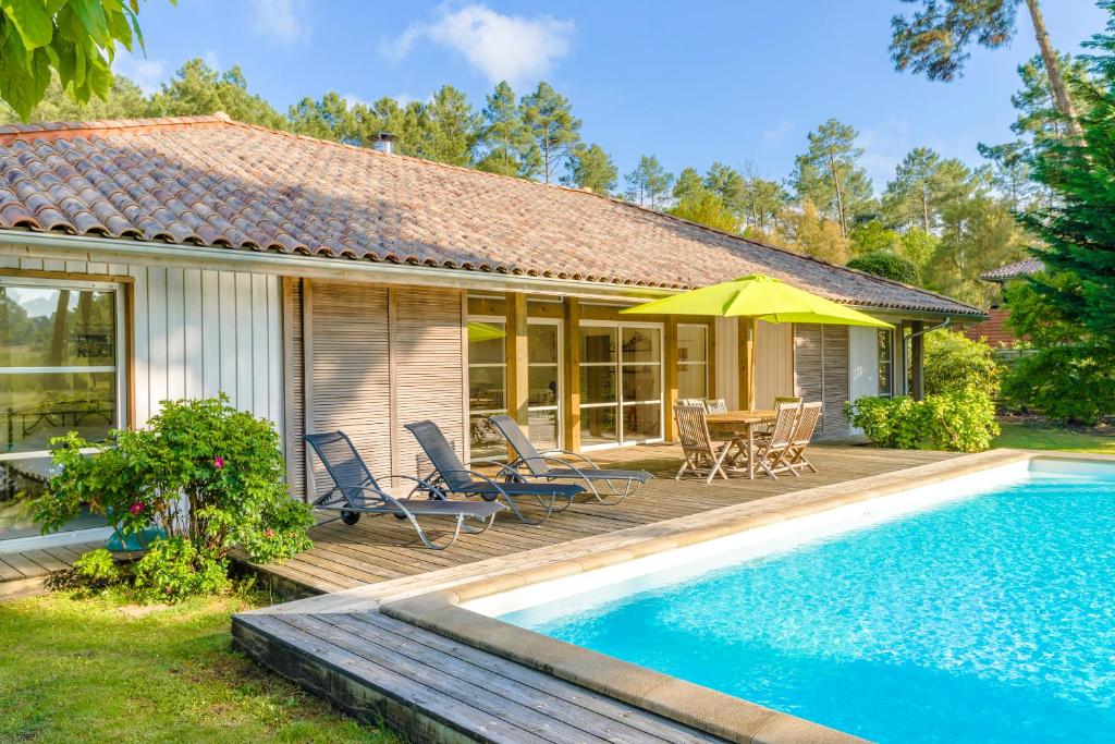 a house with a swimming pool and a patio with chairs and an umbrella at Lagrange Vacances La Clairière aux Chevreuils in Moliets-et-Maa