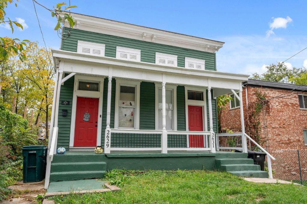 a green house with red doors and a brick building at Stylish Modern Gem in the HIlls in Cincinnati