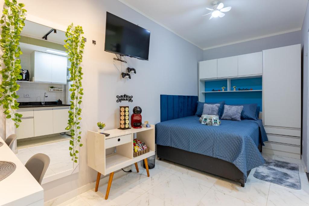 a bedroom with a blue bed and a kitchen at Manacá Studio Praticidade e Estilo na Aclimação in Sao Paulo