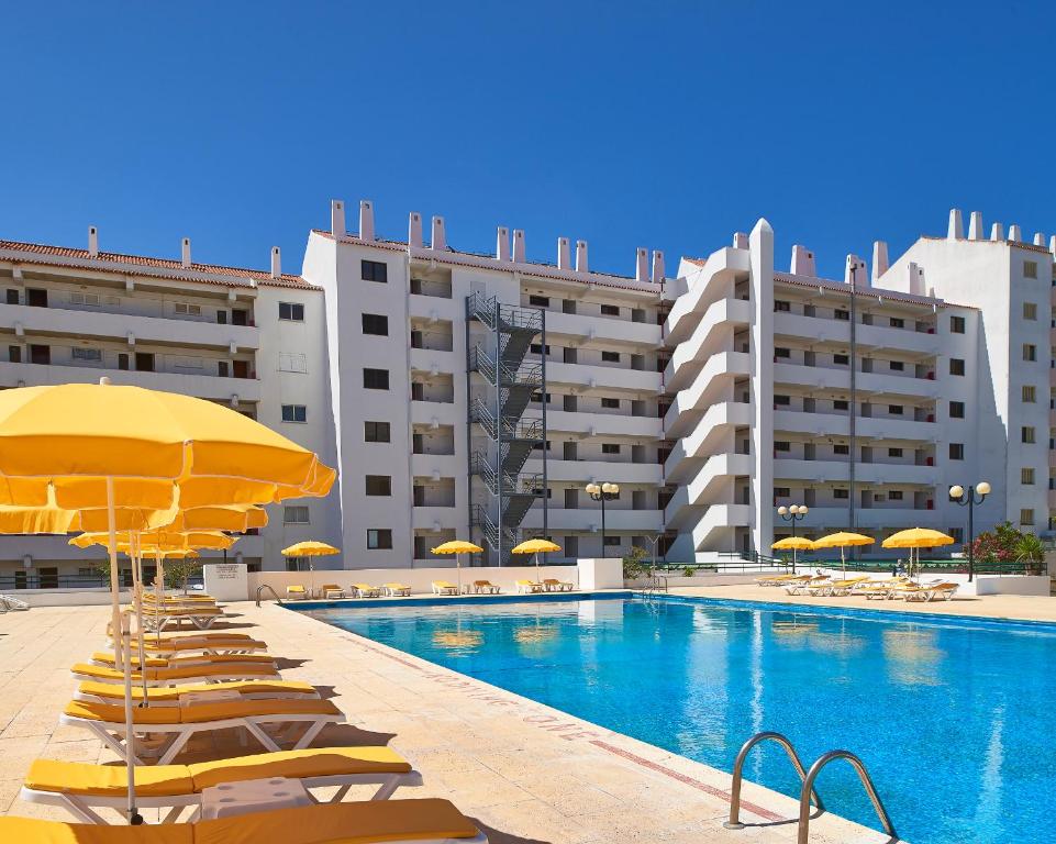 a swimming pool with chairs and umbrellas and buildings at Cheerfulway Minichoro Apartamentos in Albufeira