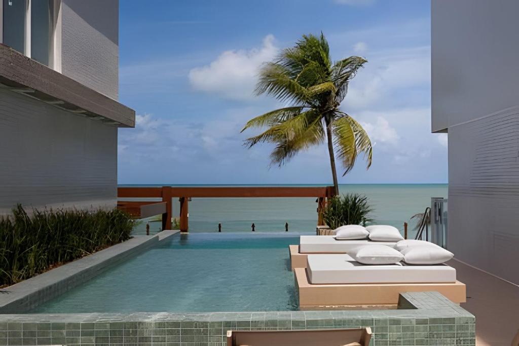 a resort pool with two beds and a palm tree at Flat pé na areia c/vista 406B Branco Haus -MyFlats in Tambaú