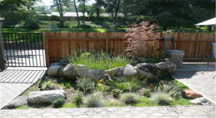 a garden with rocks and plants in front of a fence at Queen's Inn By The River in Oakhurst