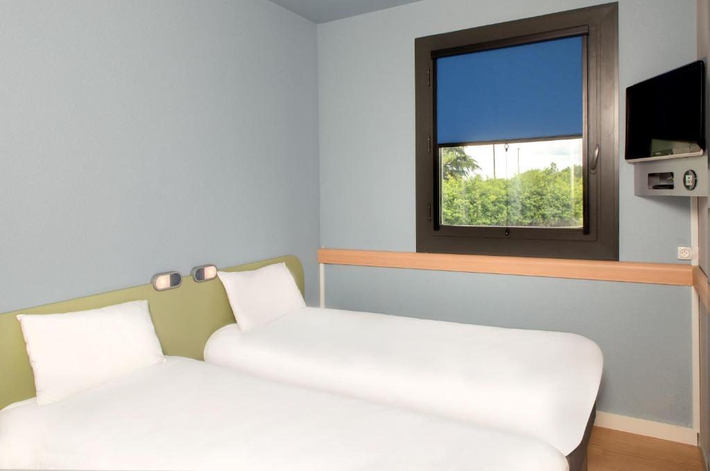 two beds in a room with a window at ibis budget Montceau les Mines in Montceau-les-Mines