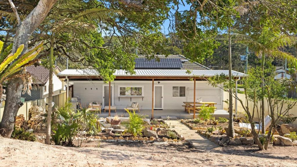 a white house with a garden in front of it at Cute Beach Cottage - Absolute Beach Front in Toukley