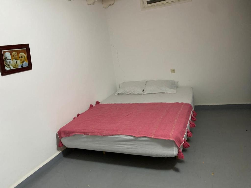 Cama en habitación blanca con manta roja en اوناغة الصويرة, en Essaouira