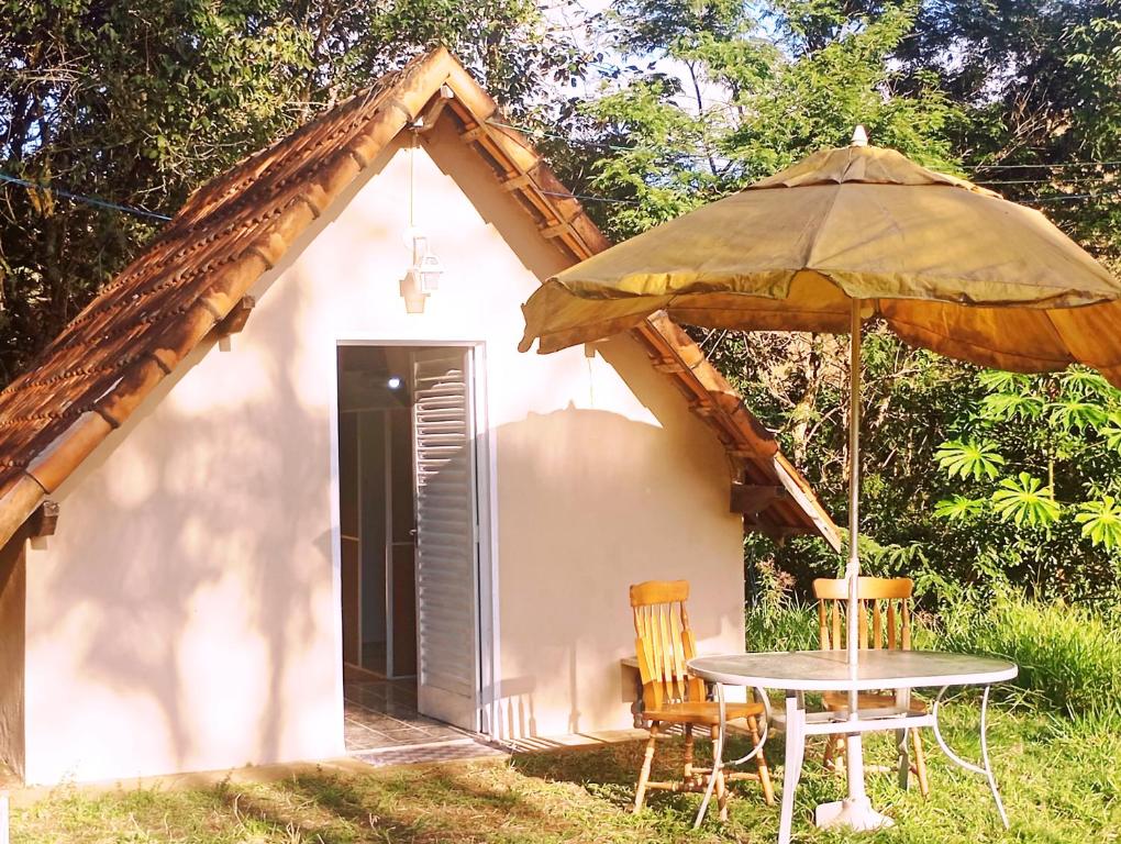 a small cottage with a table and an umbrella at Chalé Rosa Chalezinho da Serra in Natividade da Serra