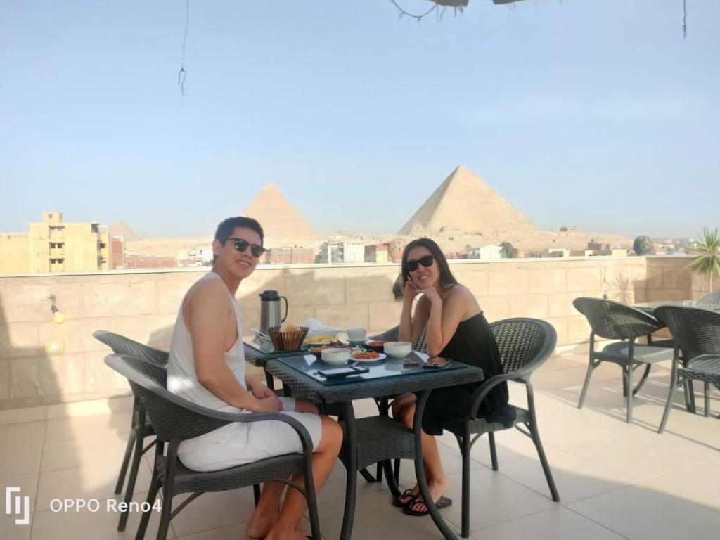 duas pessoas sentadas numa mesa com pirâmides ao fundo em Hassan Pyramids Hotel&Rooftop em Cairo