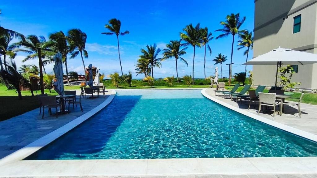 ein Swimmingpool mit Stühlen und Sonnenschirmen neben einem Gebäude in der Unterkunft Brisa Muro Alto - Flat na Praia in Ipojuca