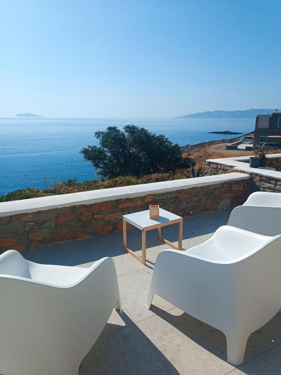 a group of white chairs and a table and the ocean at Iliada Suites Simousi Kythnos in Kithnos