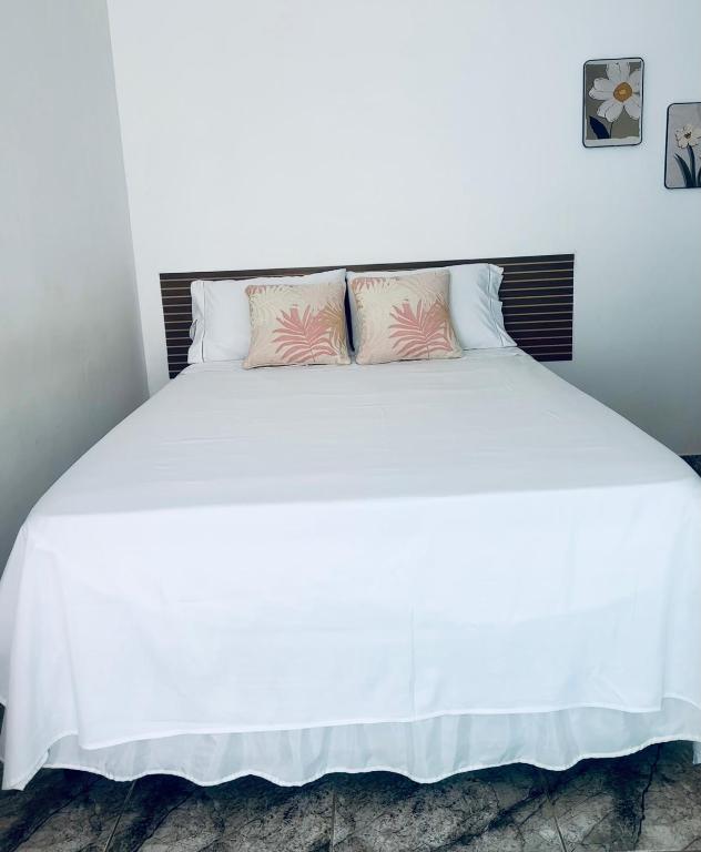 a white bed with two pink pillows on it at FRAN's - HOSPEDAGENS in Lagoa Santa