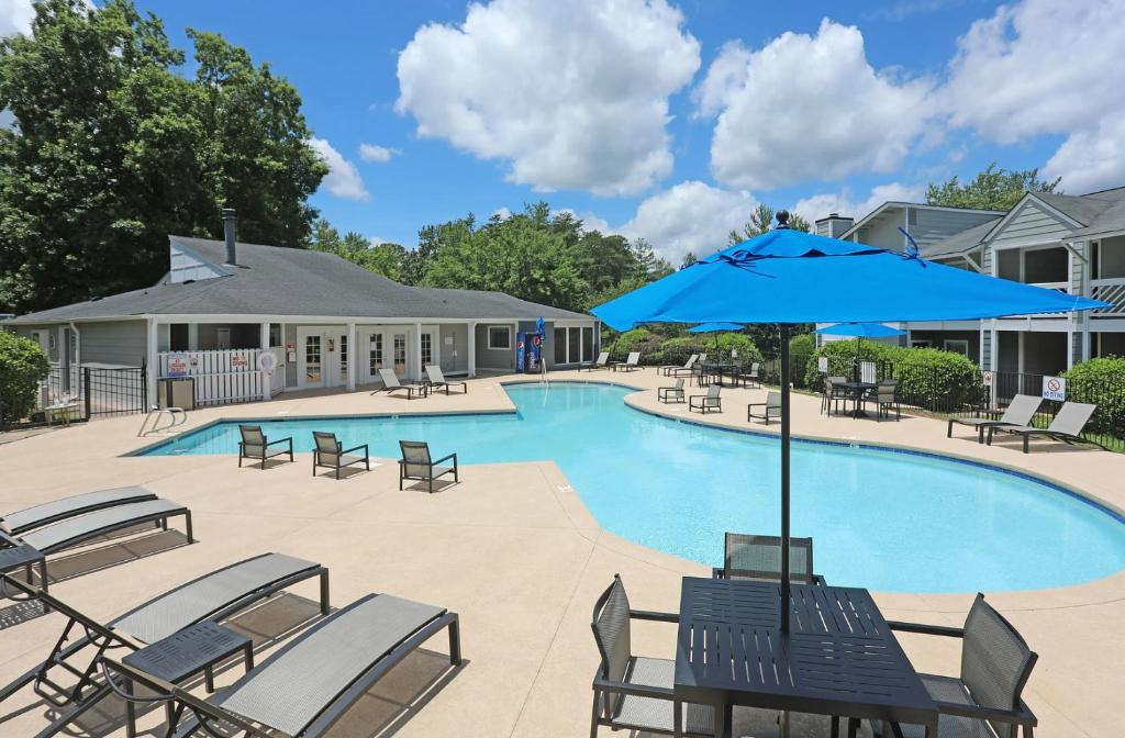 a pool with chairs and a blue umbrella at Landing Winston-Salem near Wake Forest University in Winston-Salem