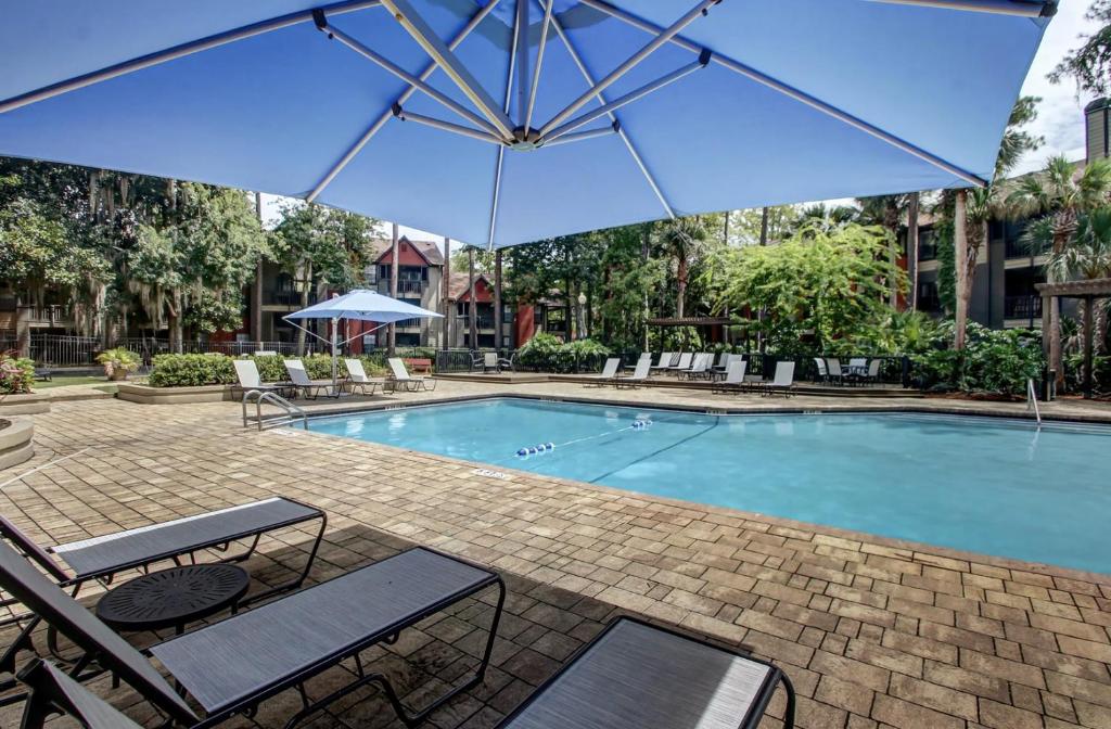 a swimming pool with chairs and an umbrella at Landing Apartments - Jacksonville in Jacksonville