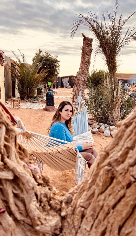 a woman sitting in a hammock in the desert at Eco Merzouga luxury camp in Merzouga