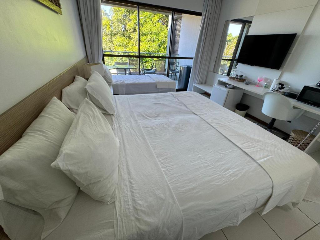 un grand lit blanc dans une chambre avec une fenêtre dans l'établissement The Experience Iloa Residenci, à Barra de São Miguel