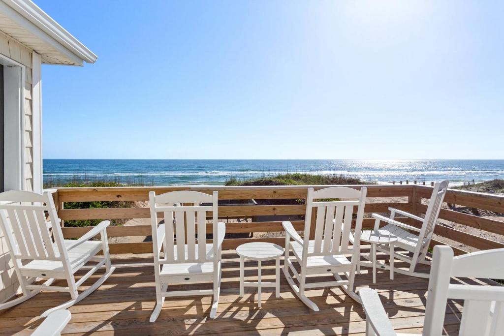 a group of white chairs on a deck with the beach at 6175 - Longview Cottage in Whalebone
