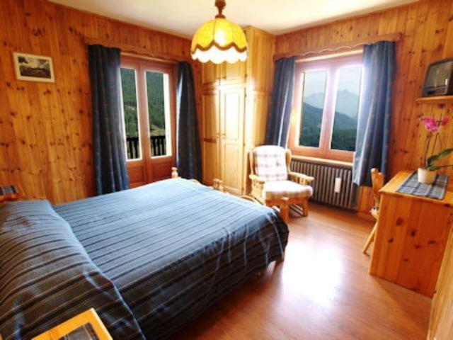 um quarto com uma cama, uma cadeira e janelas em Hotel Alpe Fleurie em Champoluc