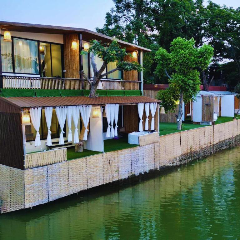 a resort on the water with tables and umbrellas at Baanrimnam Resort Lopburi in Chai Badan