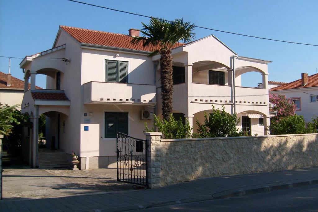 a white house with a palm tree in front of it at Apartments Aurora Borik in Zadar