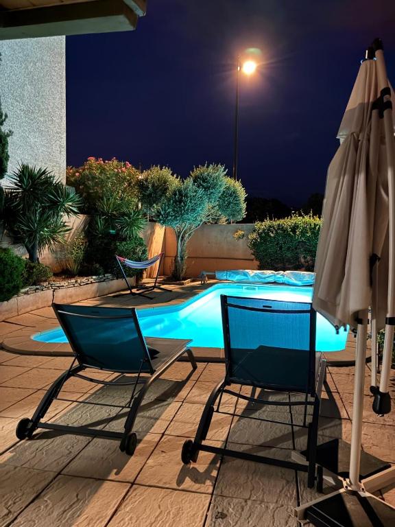 - deux chaises et un parasol à côté de la piscine la nuit dans l'établissement RIBA D'AUDE SPA privatif proximité aéroport et de la Cité médiévale, à Carcassonne