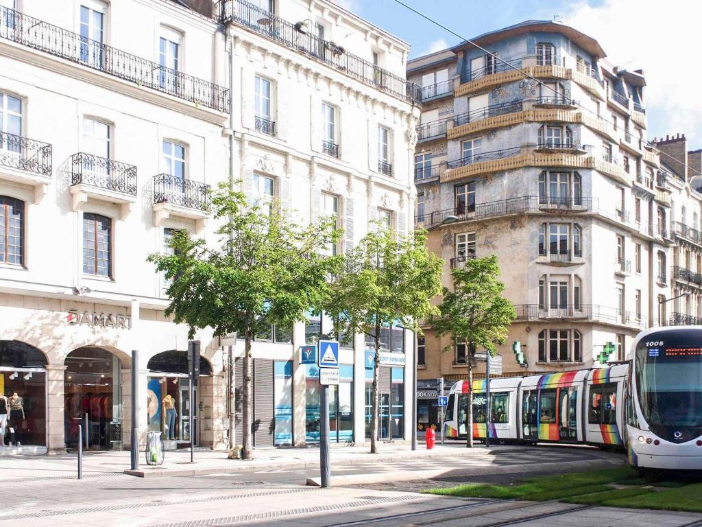 Un autobús que circula por una calle junto a edificios altos. en Mercure Angers Centre Gare, en Angers