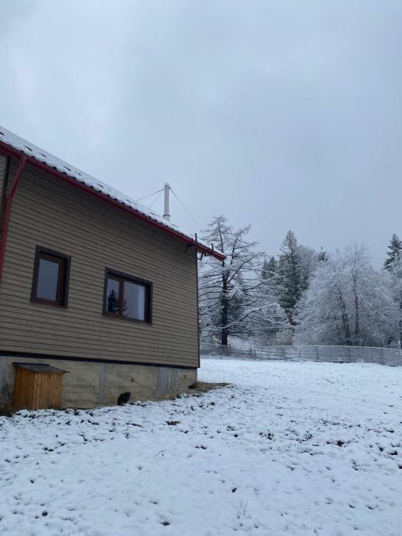 een huis met sneeuw op de grond naast een gebouw bij Hutsulka House in Mykulychyn