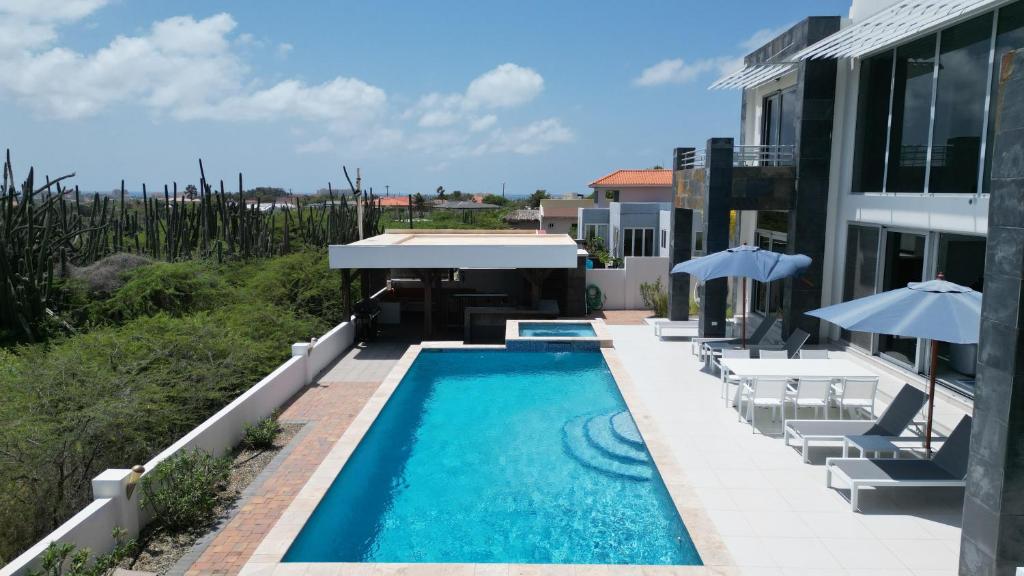 a swimming pool with chairs and umbrellas next to a house at Ocean View Mansion 8 min to Palm Beach in Noord