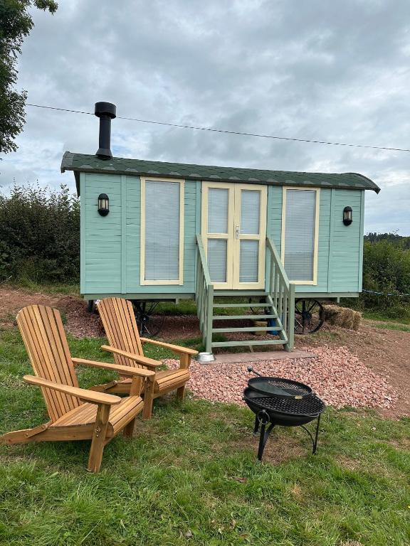 a green tiny house with two chairs and a grill at Secret Valley Shepherds Hut in Llanfaenor