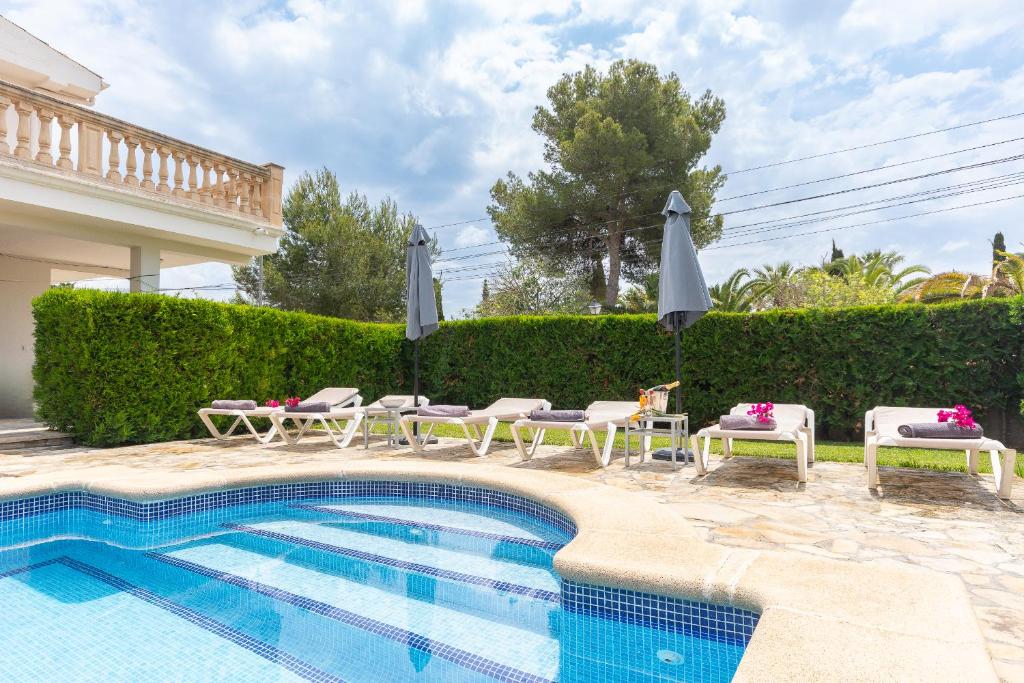 a swimming pool with lawn chairs and an umbrella at Chalet Muro en Mallorca in Playa de Muro