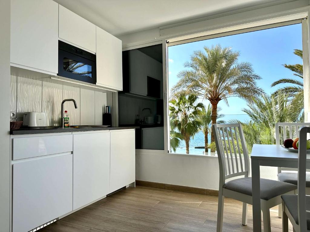 a kitchen with white cabinets and a table and a large window at Neues Studio direkt am Strand in Arguineguín