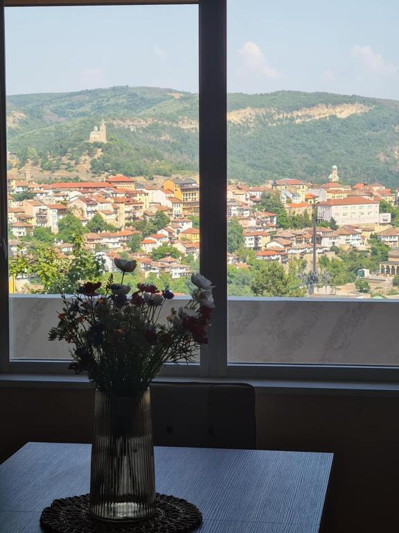 a vase with flowers on a table in front of a window at Апартаменти Ванкови in Veliko Tŭrnovo