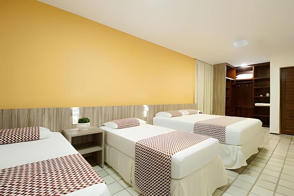 Zimmer mit 3 Betten und gelber Wand in der Unterkunft Mansão14Suítes-55Pessoas-BEACH PARK - HOUSINGCEARÁ in Aquiraz