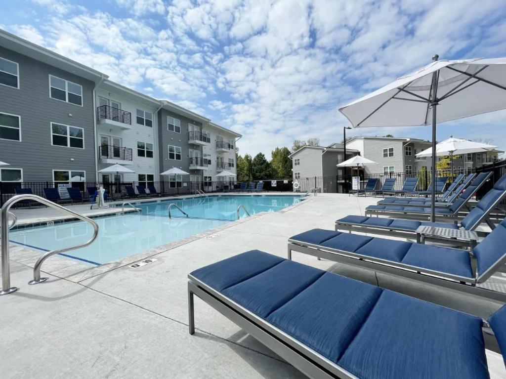 einen Pool mit blauen Stühlen und einem Sonnenschirm in der Unterkunft North Concord Apartments by Landing in Kannapolis